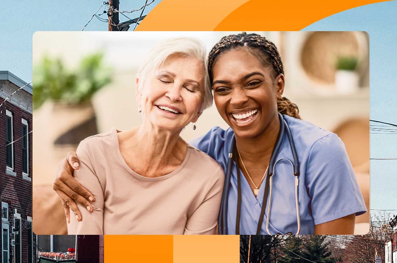A young Black nurse sits side-by-side with an elderly white woman. The nurse has her arm around the older woman's shoulders and the older woman is leaning into the embrace. Both are laughing and comfortable together, like they have known each other for a long time. The backdrop is of a city neighborhood.